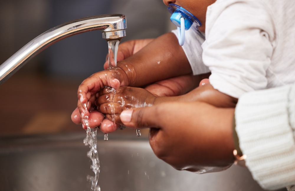 The littlest hands need the biggest help. Shot of an unrecognisable woman washing her babys hands in the sink at home.